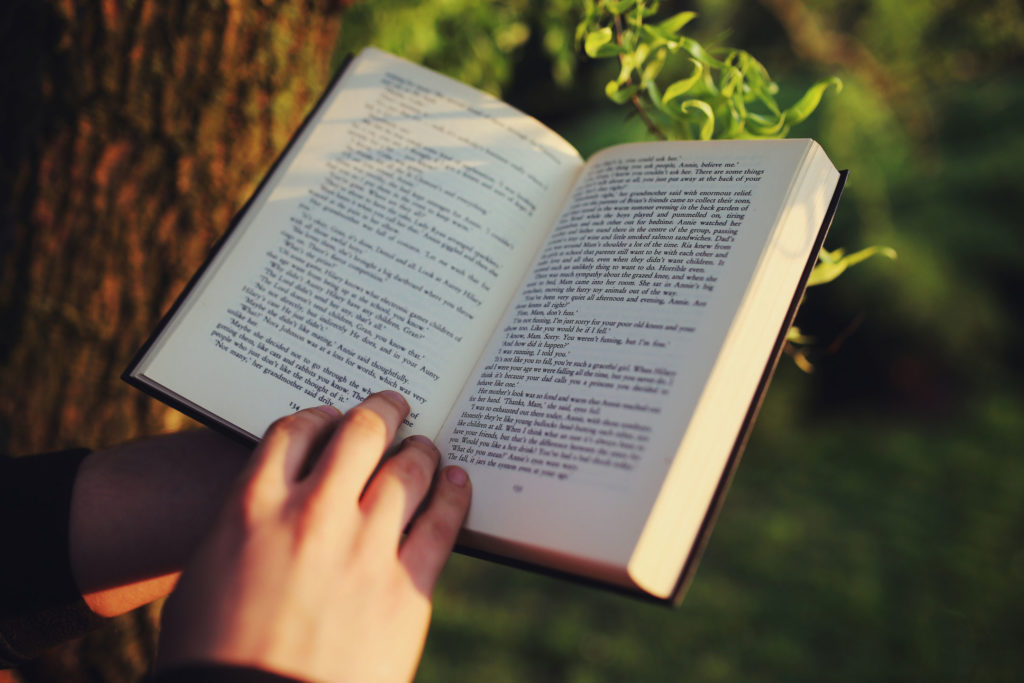 Lettura di un libro in mezzo al verde. Primo piano sul libro e sulle mani